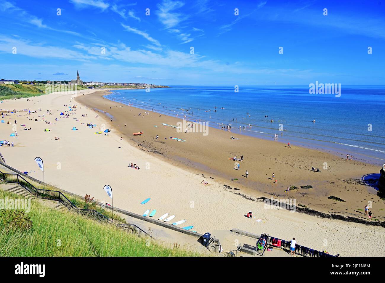 Glorious sunny blue sky calm August day on Tynemouth Long Sands at low tide with surfers canoes boarders and swimmers and families Stock Photo