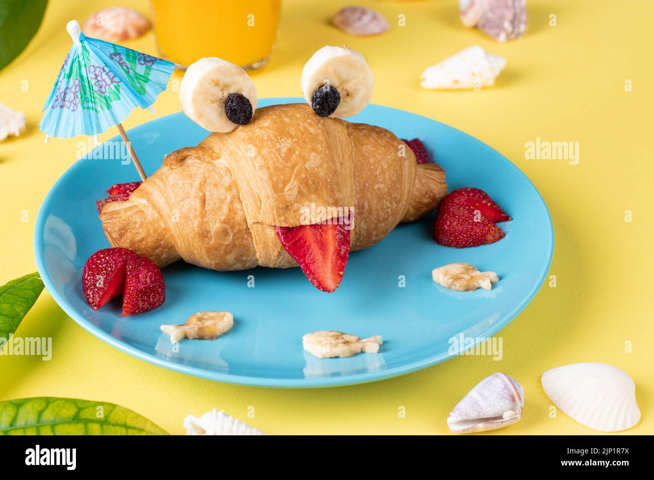 Fun food for kids - crab shaped croissant with strawberry and banana on yellow background Stock Photo