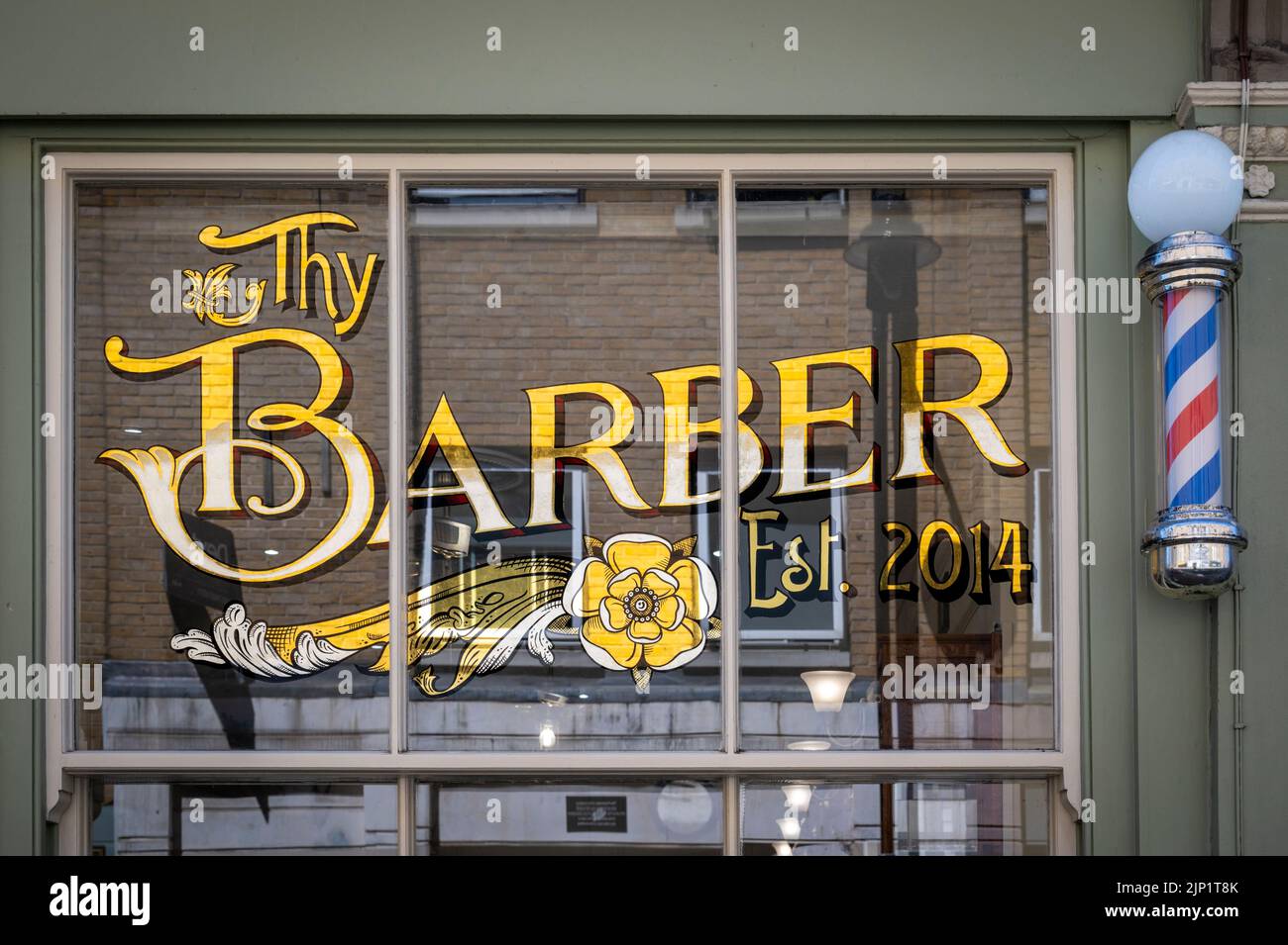 Thy Barber, barbers shop window with ornate gold painted window sign and barbers pole Spitalfields London UK Stock Photo