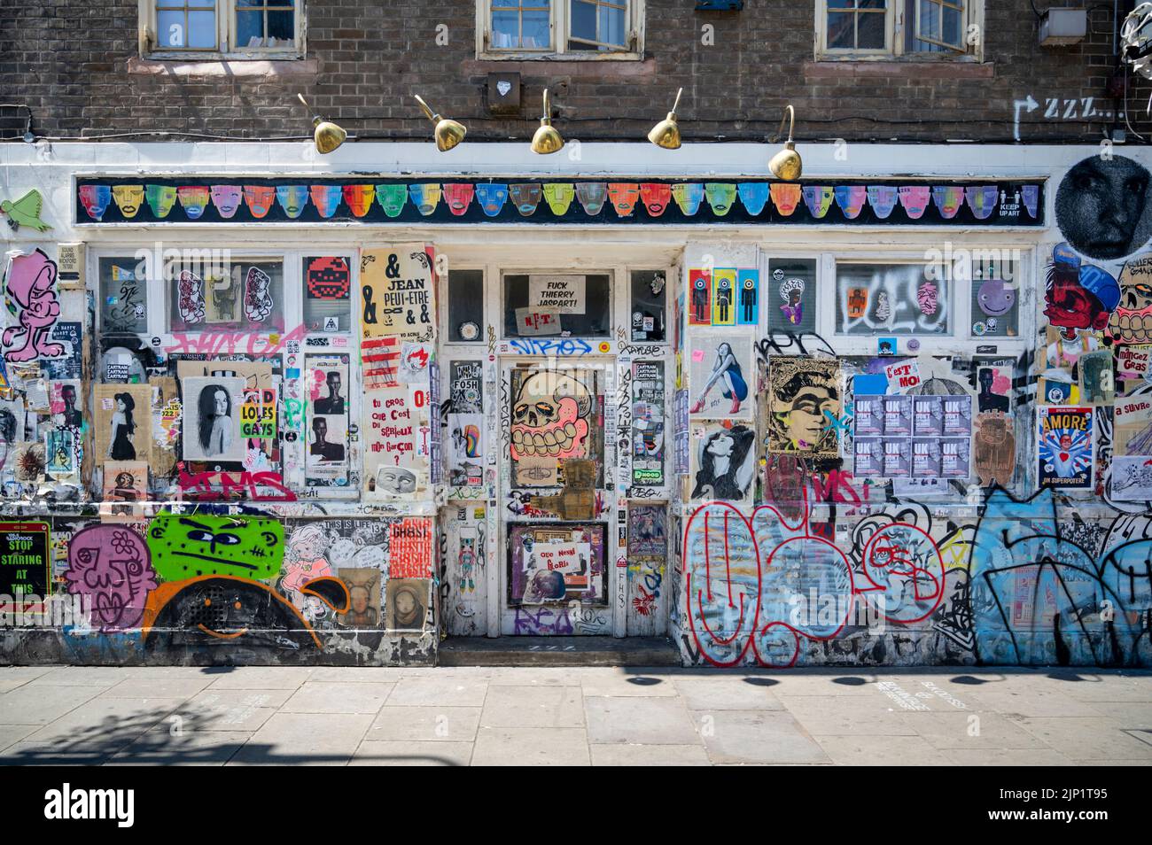 A shop front covered in colourful posters and grafitti in Brick Lane London Uk Stock Photo