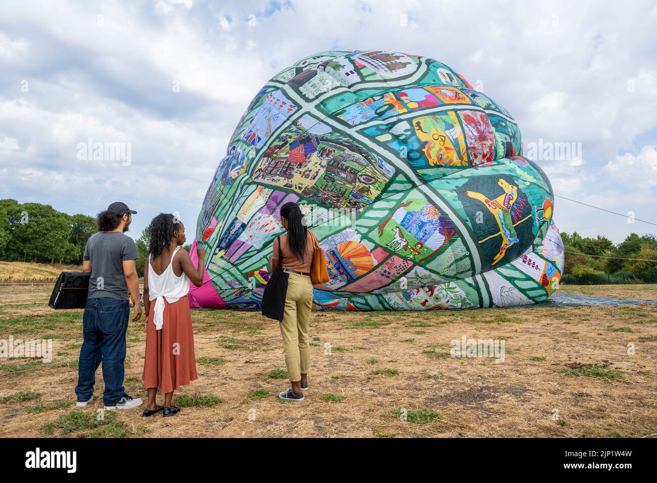 London, UK.  15 August 2022. People view a new artwork ‘Fields of EveryWhen’ by artists Neil Musson & Jono Retallick, Thamesmead Open art prize winners, organised by Peabody, being semi inflated.  The 25 metre high hot air balloon features 200 artworks celebrating the people and places of Thamesmead which will fly five times above Thamesmead until the end of September, including the Thamesmead Festival.  As well as floating overhead the balloon can be inflated to create an installation that visitors can walk inside to view the artworks up close.  Credit: Stephen Chung / Alamy Live News Stock Photo