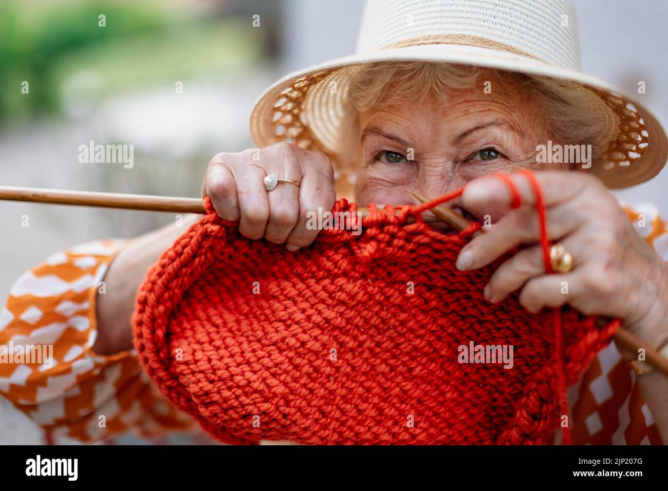 Portrait of senior woman sitting outdoor and knitting red scarf. Stock Photo
