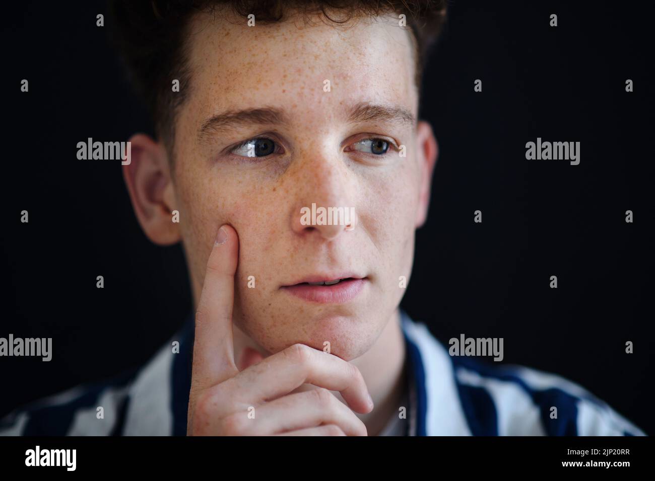 Portrait of thoughtful handsome young man with ginger hair and freckles looking away on black background, close-up Stock Photo