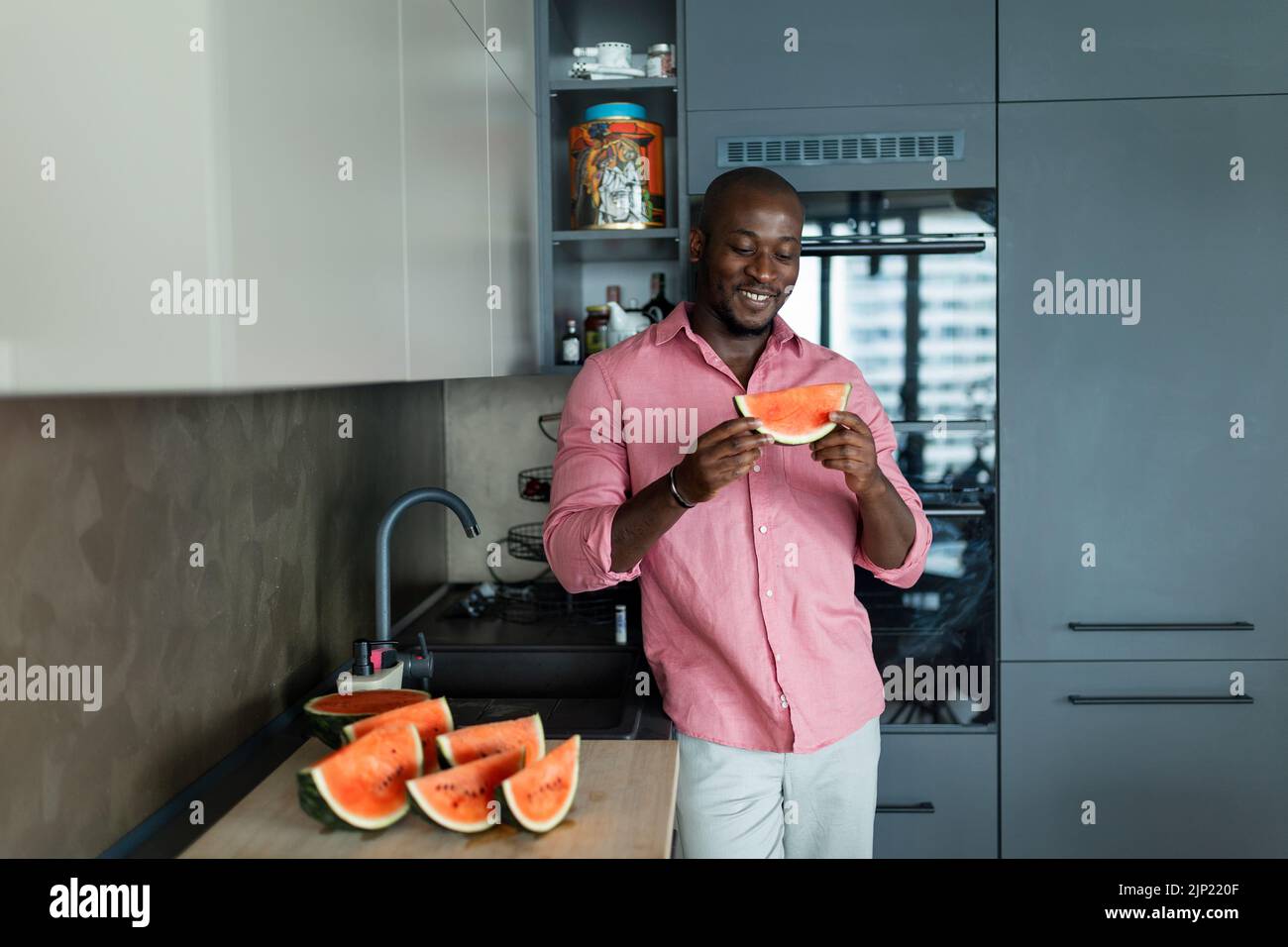 Multiracial man eating watermelon in his kitchen during hot sunny days. Stock Photo