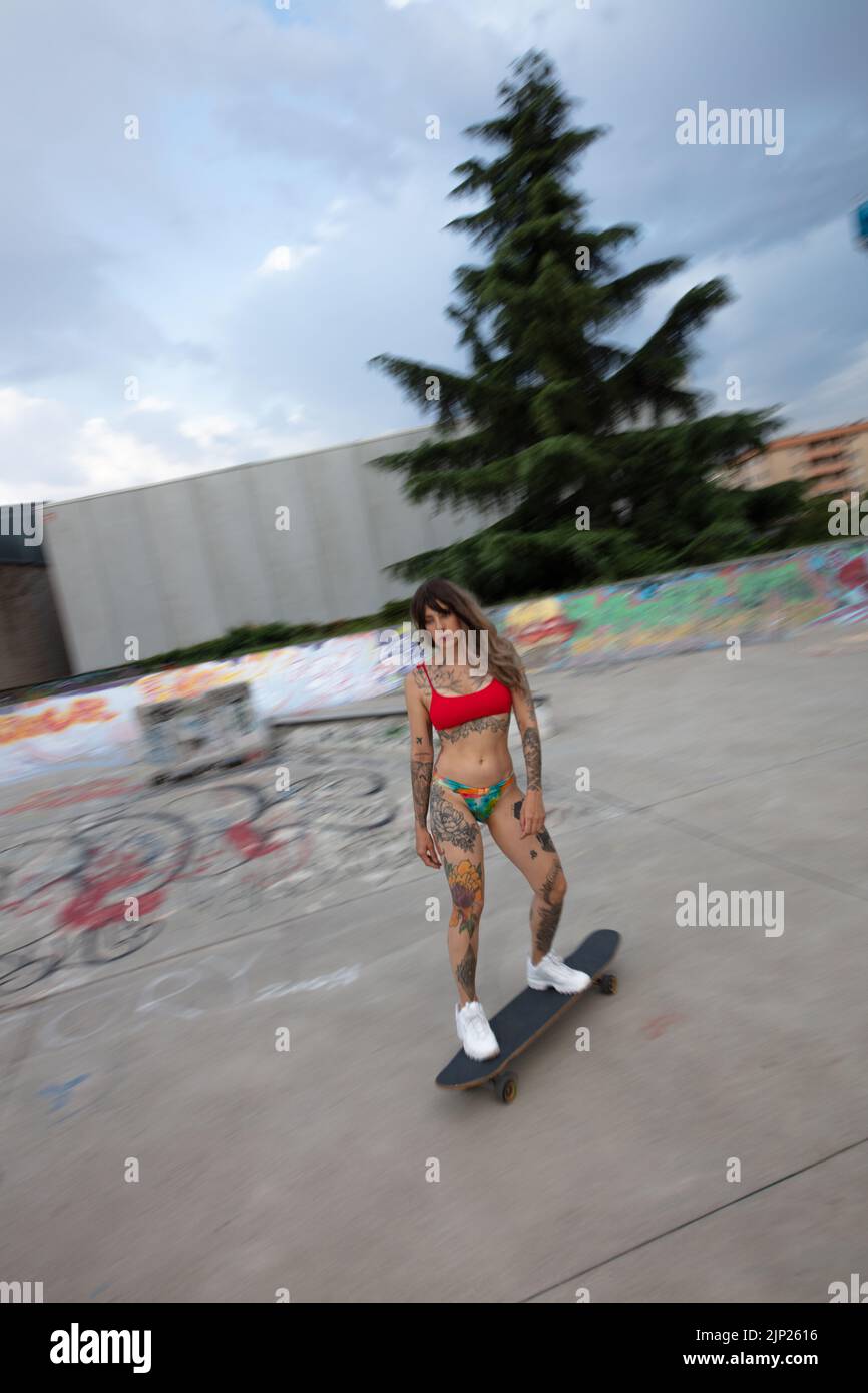 a beautifull tattooed model with skateboard/longboard, in bikini, skateboarding at the skatepark Stock Photo