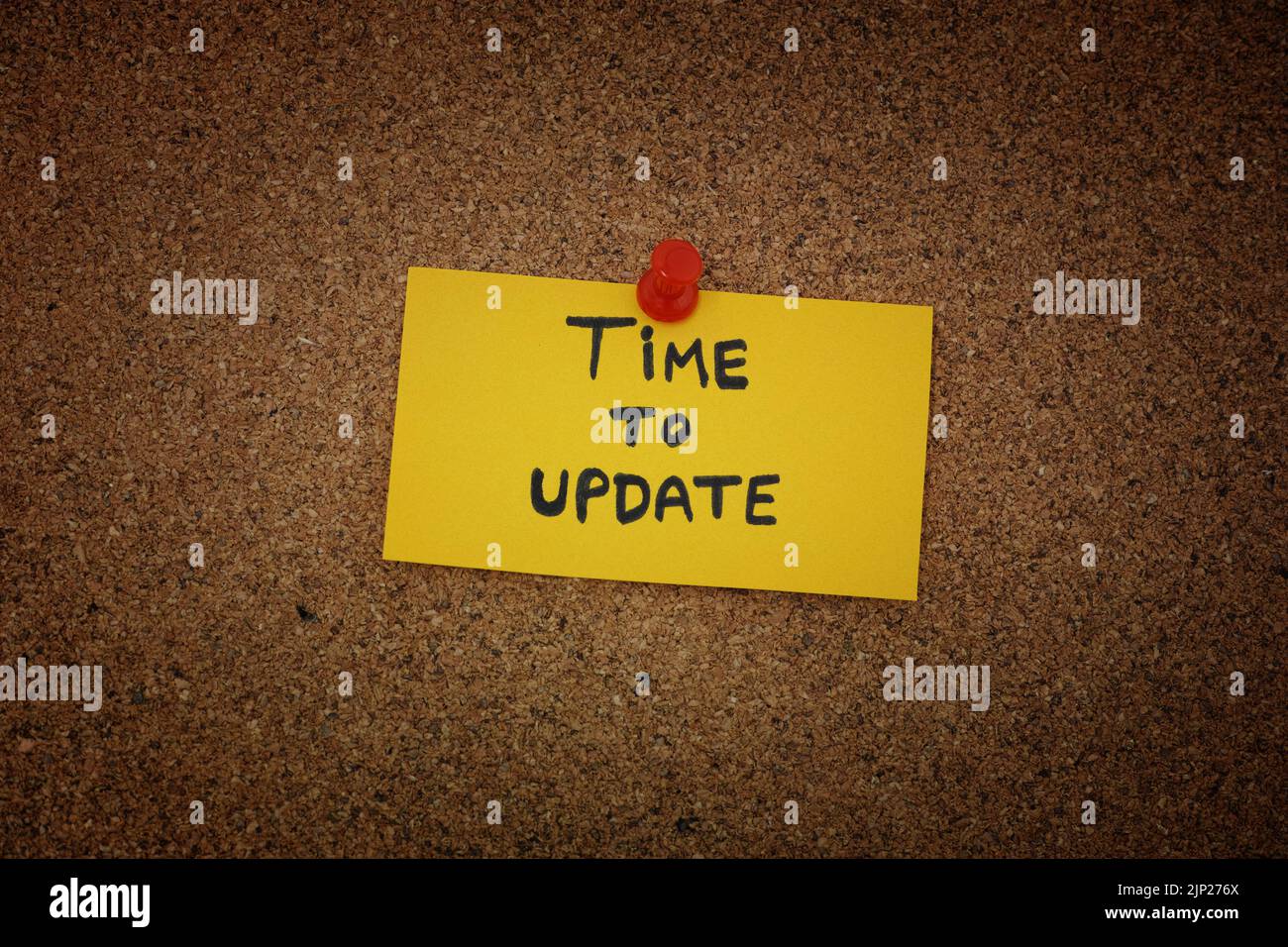 A yellow paper note with the words Time to Update on it pinned to a cork board. Close up. Stock Photo