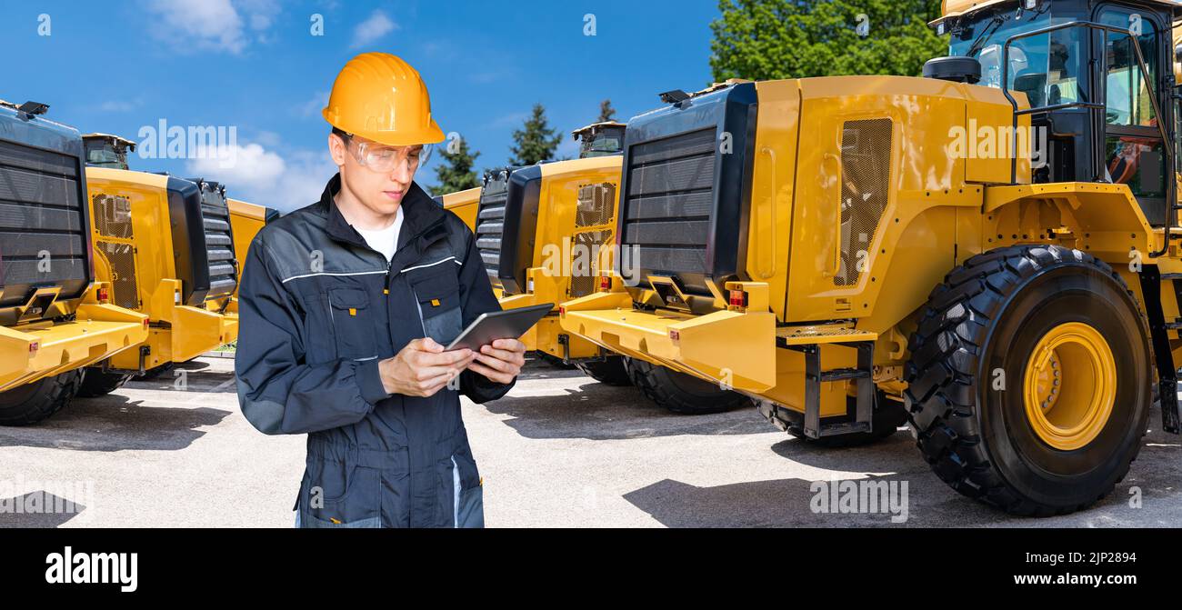 Engineer in a helmet with a digital tablet on the background of construction machines Stock Photo