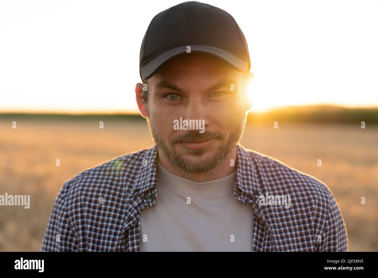 Bearded farmer in a cap and a plaid shirt against the background of a field Stock Photo