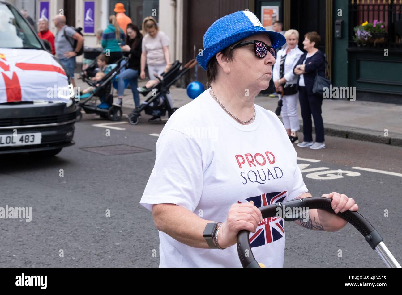 Antrim, 12th July 2022, UK. Woman wearing Ulster sunglasses and Prod Squad t-shirt walking behind one of the bands at annual Twelfth demonstation. Stock Photo