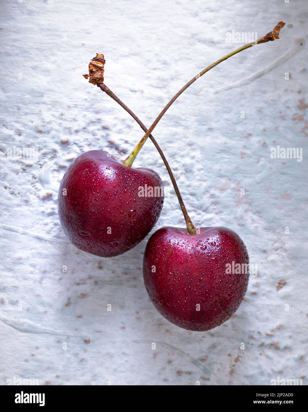 Two fresh cherries on a textured white surface Stock Photo