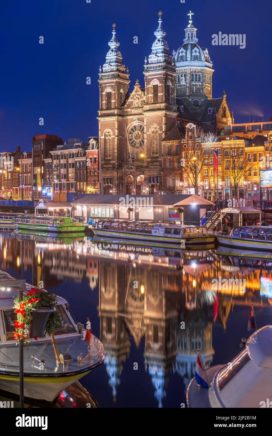 Amsterdam, Netherlands city center view with riverboats and the  Basilica of Saint Nicholas at night. Stock Photo