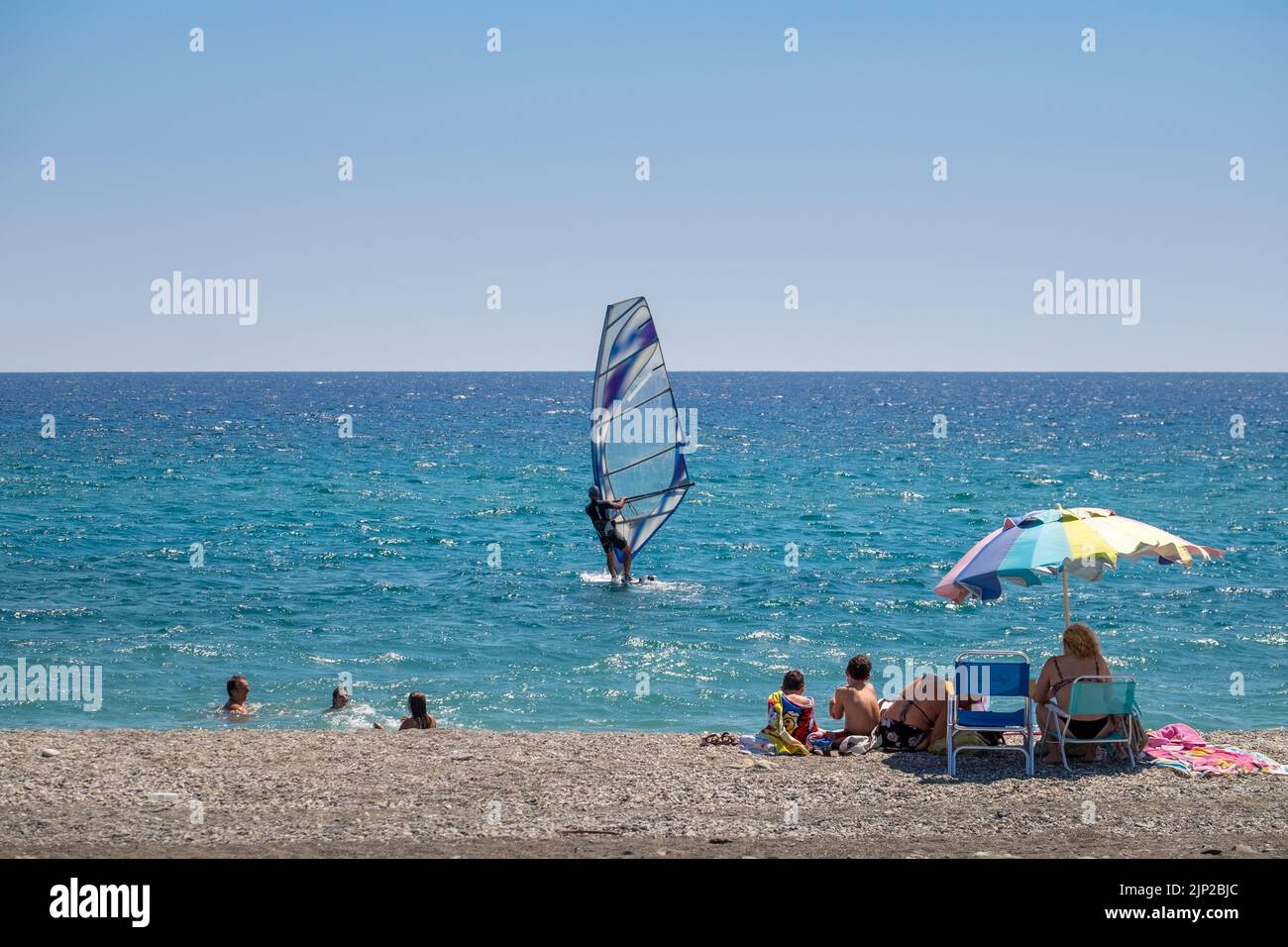 Family in the shore staring a windsurfer in the sea of Agiokampow beach ,Greece Stock Photo
