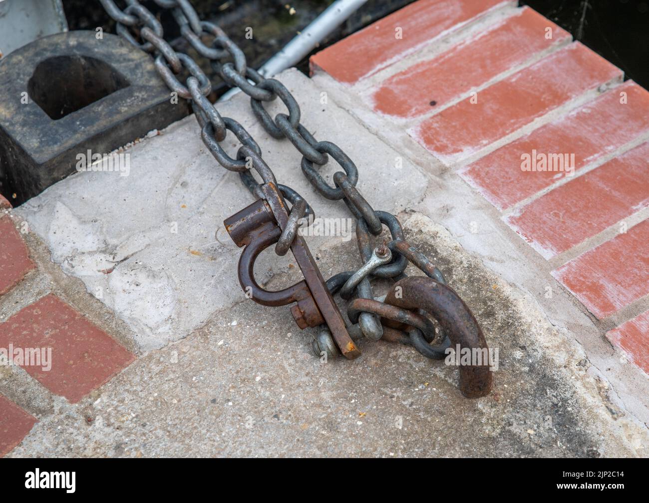 metal chain fixed to a concrete and red brick wall with D links. Stock Photo