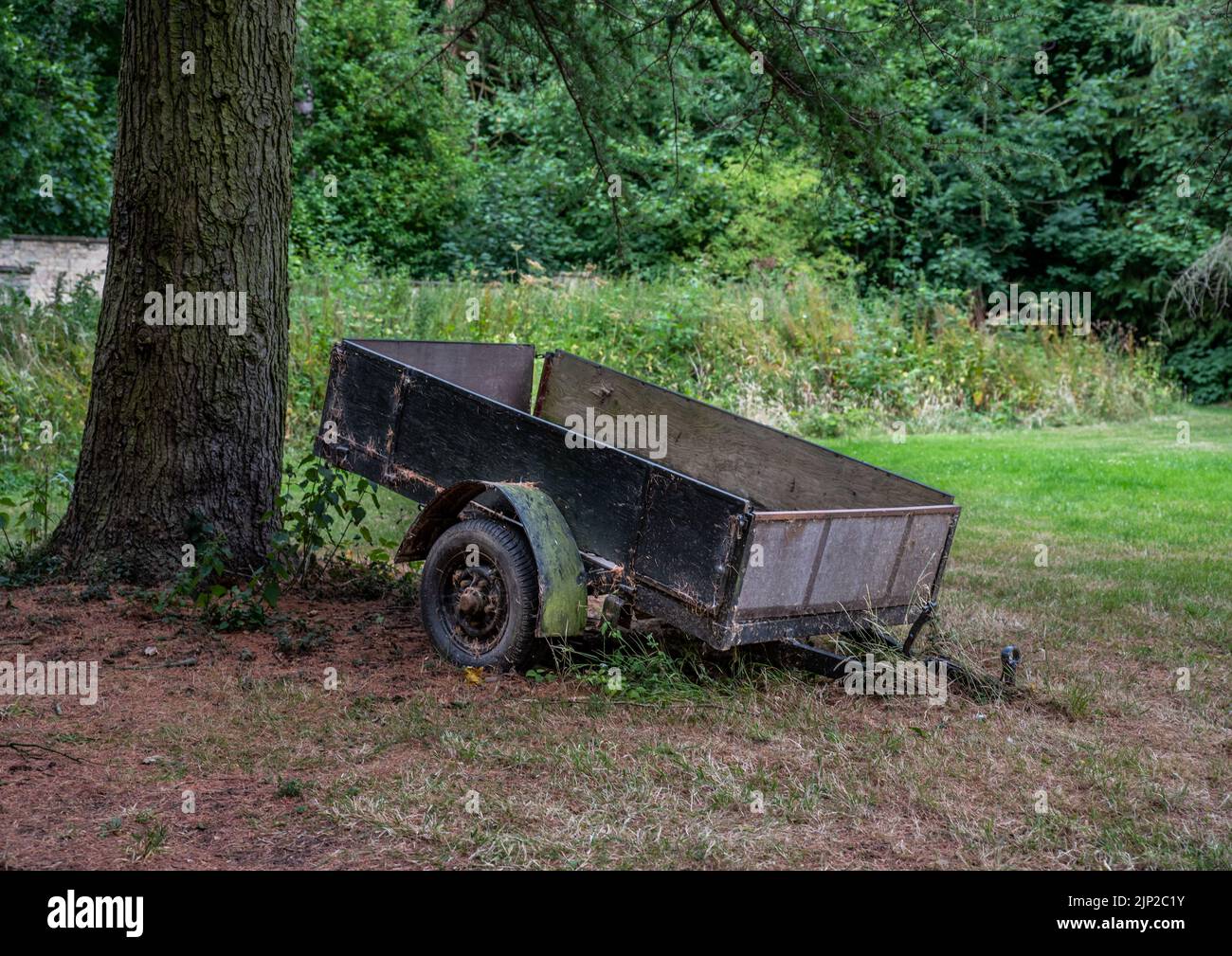 Old abandoned trailer next to a tree with over grown grass. Stock Photo