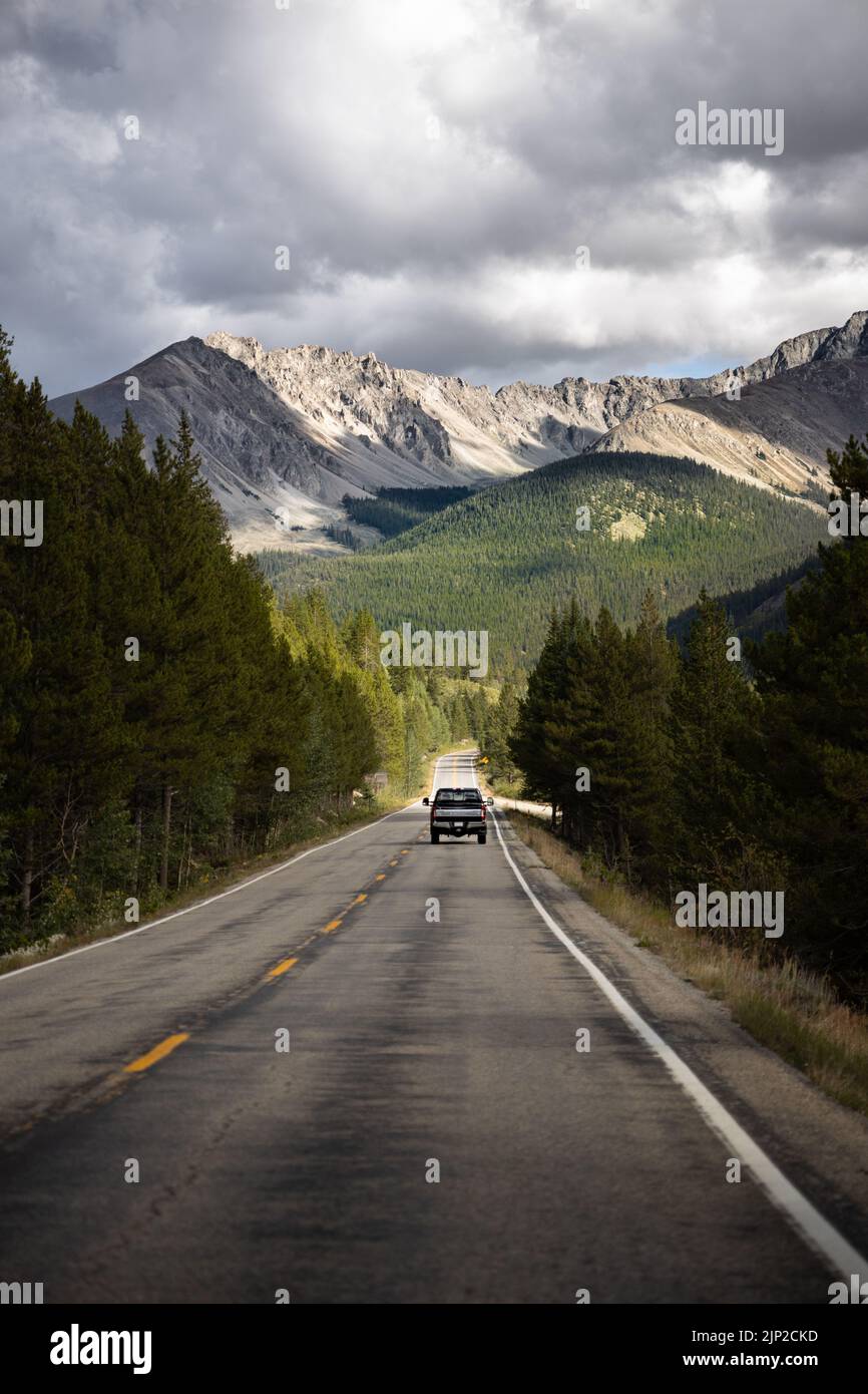 A car on the road surrounded by trees with mountains in the background ...