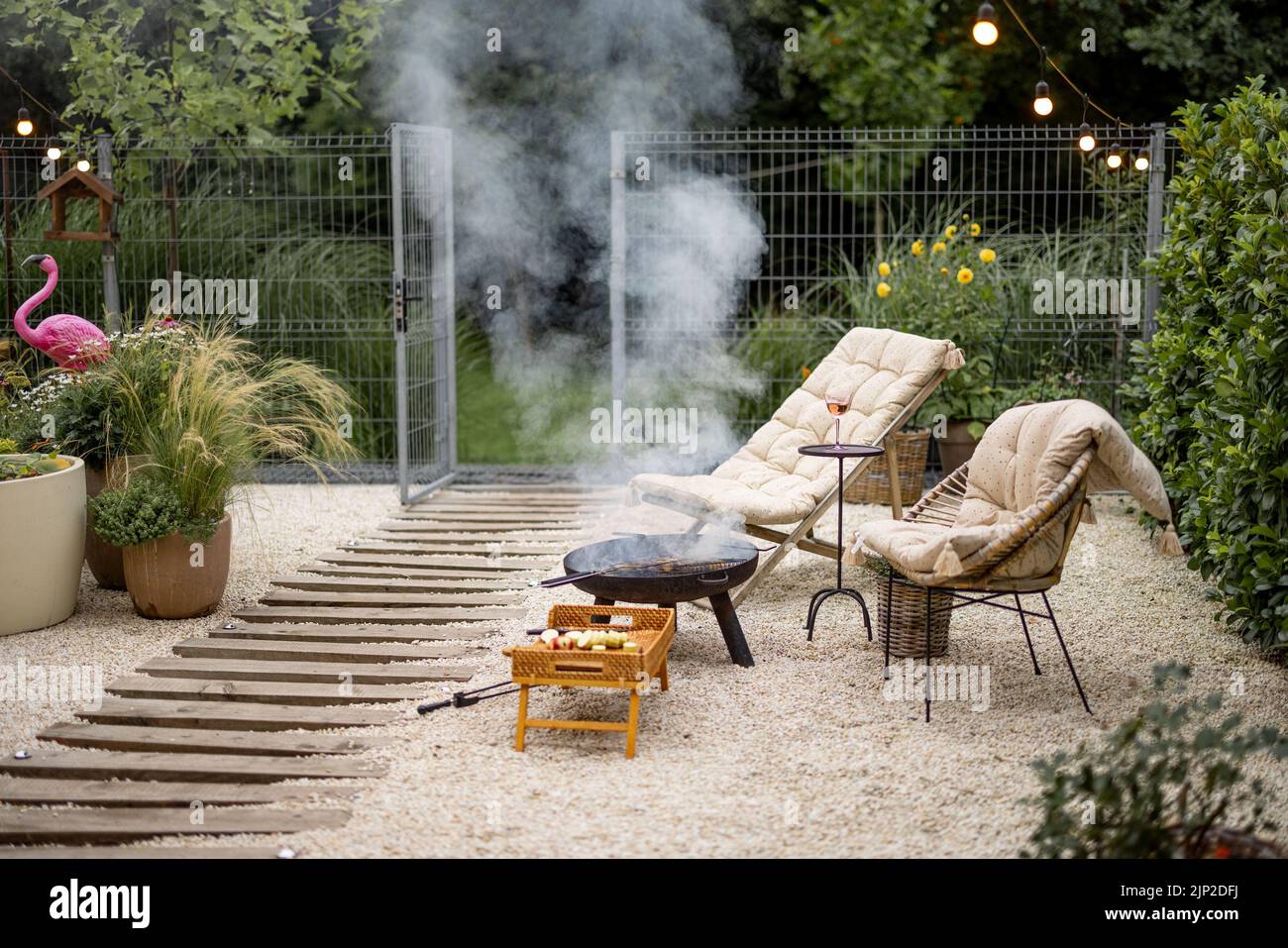 Atmospheric backyard with fire and lounge chairs at dusk on nature. Grilling food on fire bowl Stock Photo