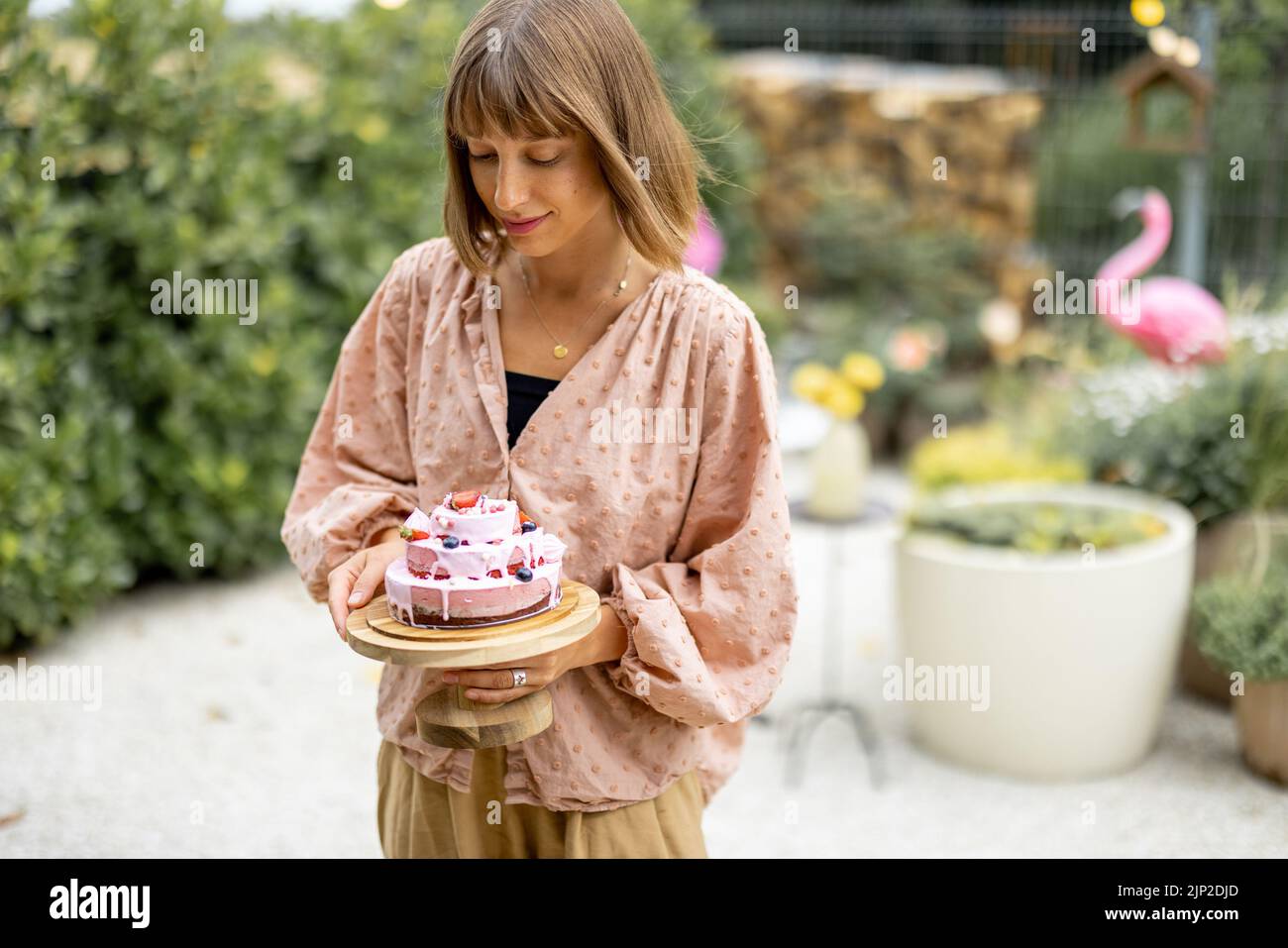 Young cheerful woman stands with festive cheesecake in garden. Happy holiday and celebration concept Stock Photo