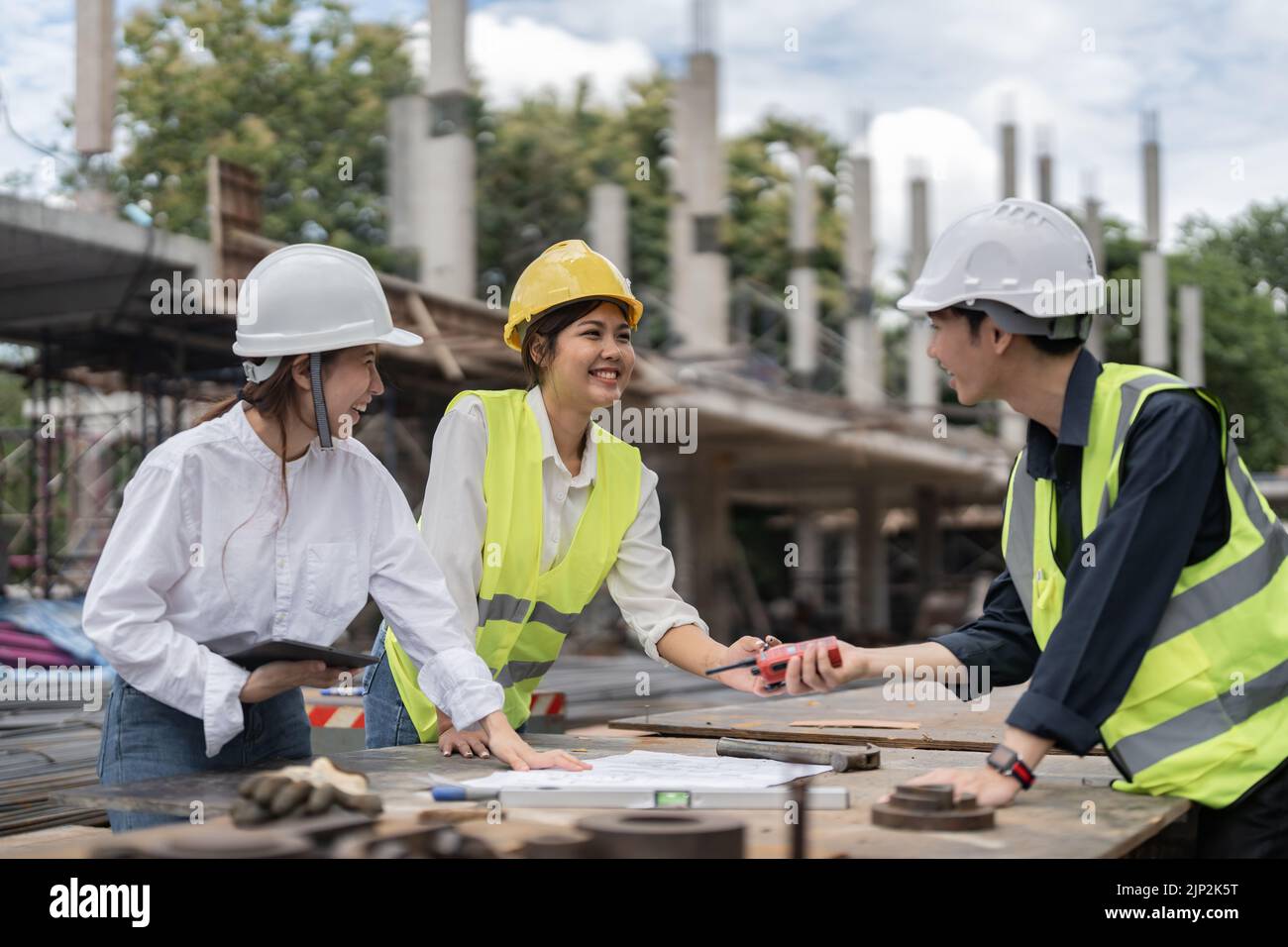 Three colleagues discussing data working and tablet, laptop with on on architectural project at construction site Stock Photo