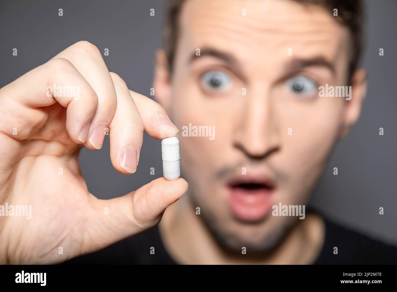 A young man look at big white capsule pill in his hand afraid to