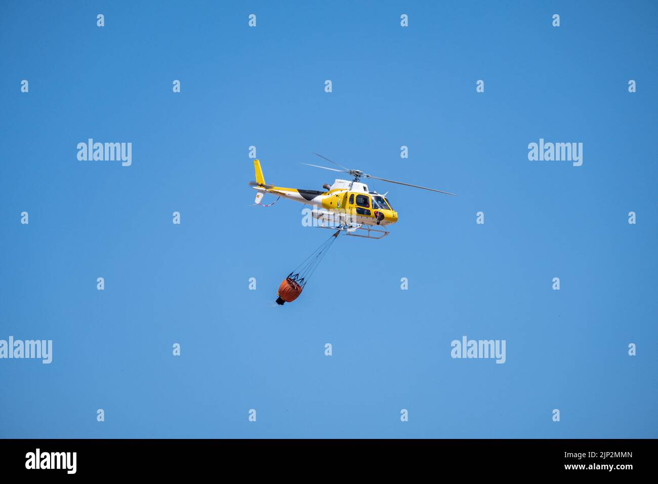 A firefighting service helicopter carrying a basket with water flying