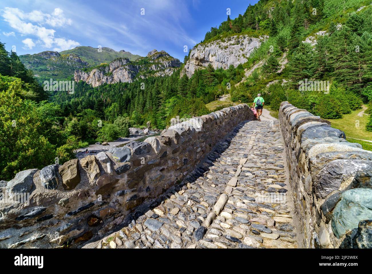 Stone bridge over river in landscape of high mountains and green forest ...