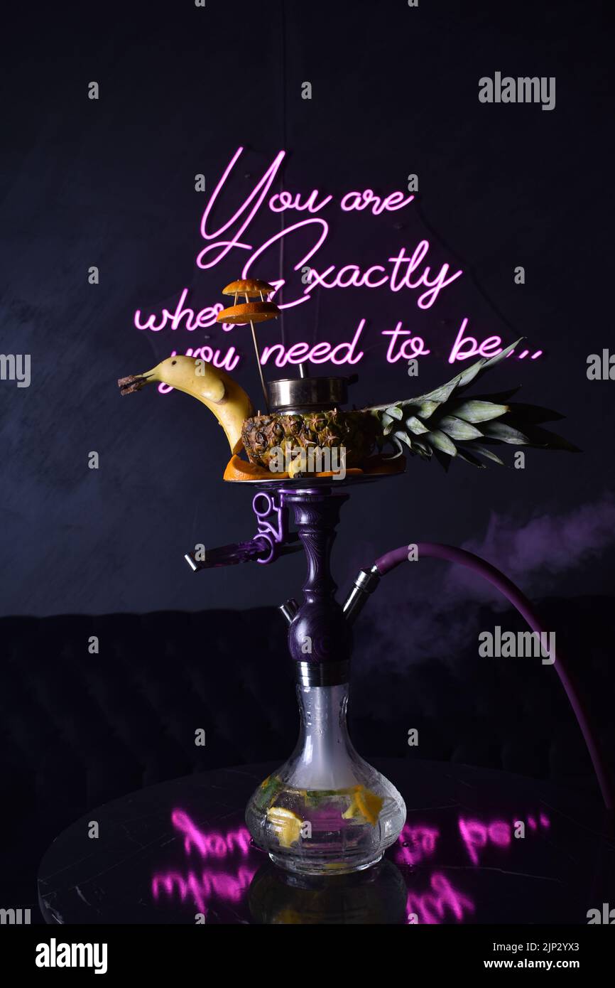 A vertical shot of a hookah with exotic fruits and motivational quote on a wall in the background Stock Photo