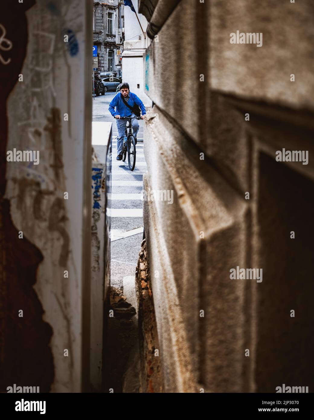 A man in a blue shirt visible from the small hole between buildings riding a bicycle on the streets of Bucharest Stock Photo