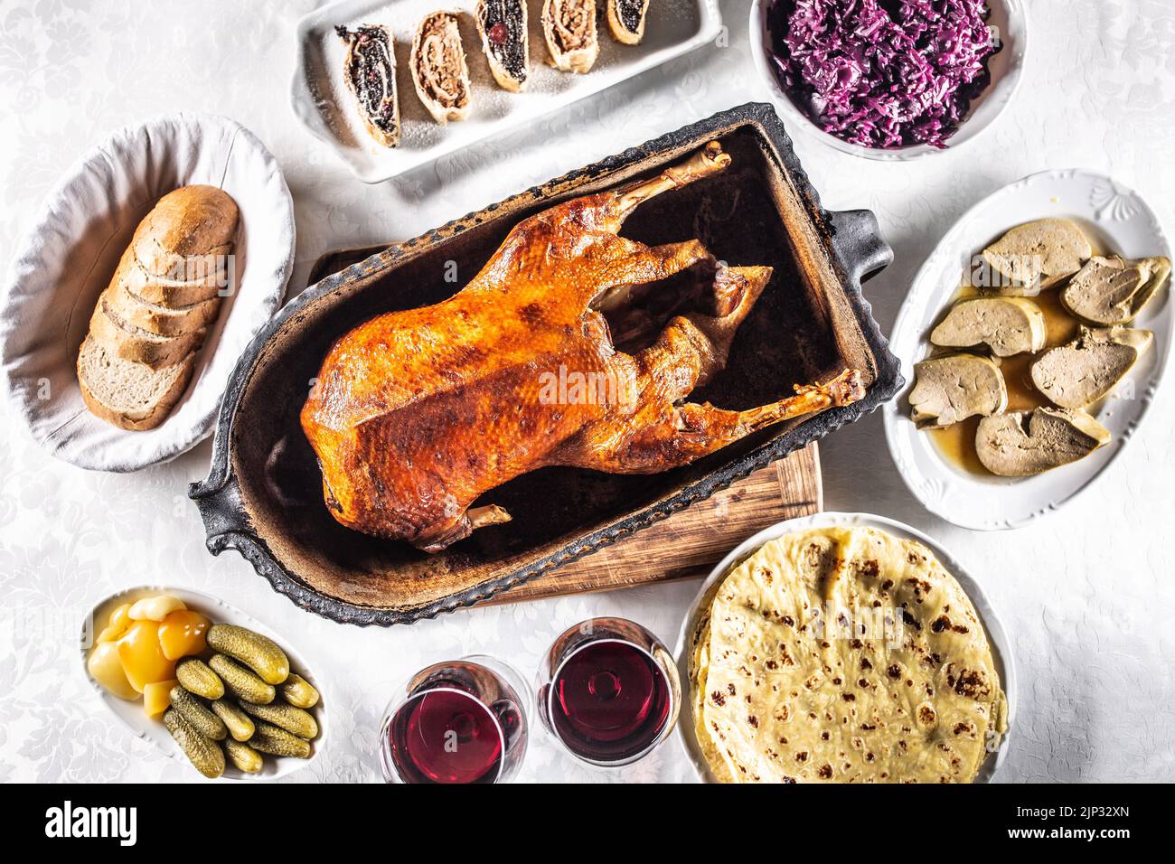 Roast goose with side dishes, red cabbage, roast, strudel, potato dumplings, pickles, bread and red wine. Traditional holiday food. Top view. Stock Photo