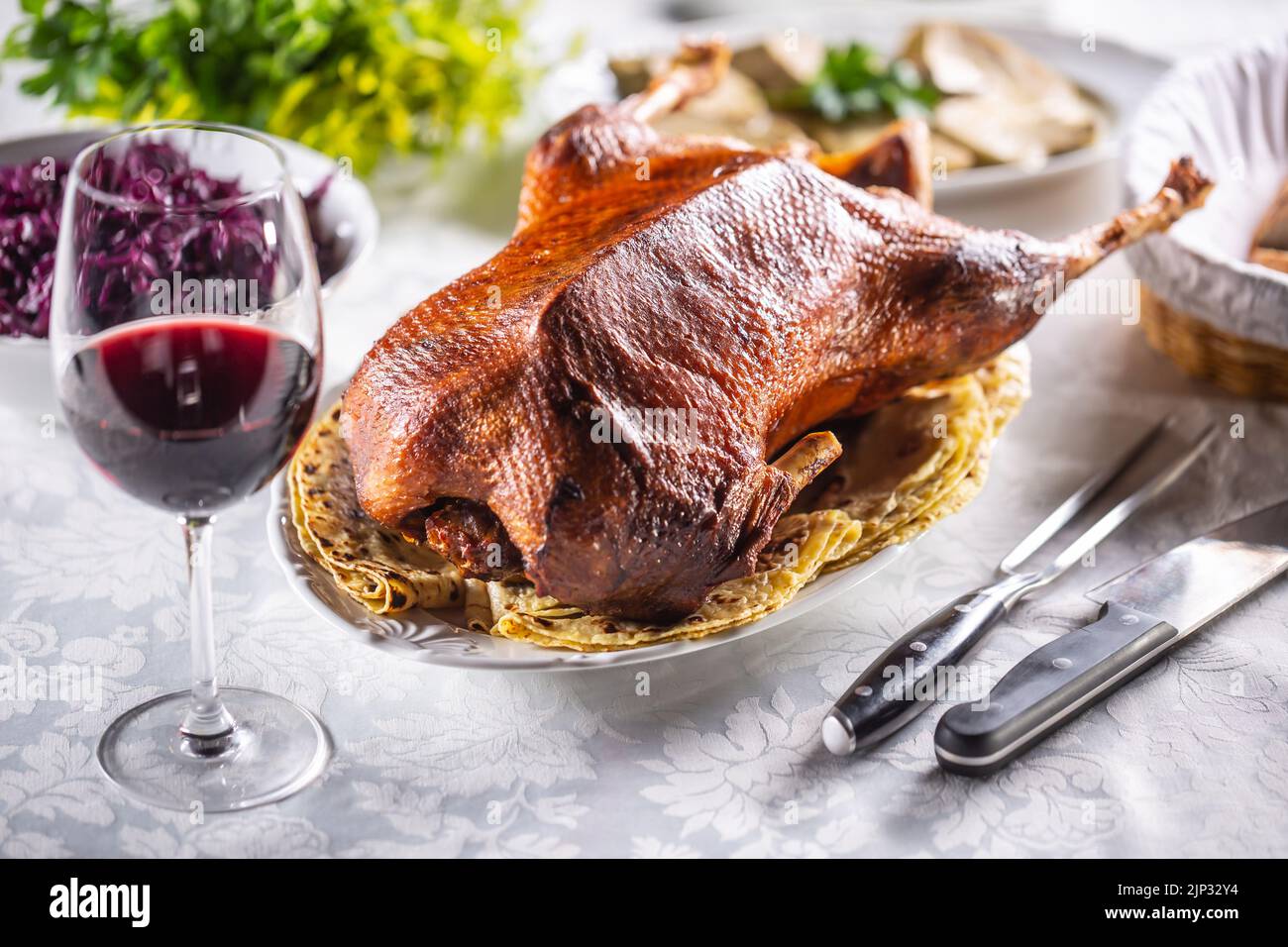 Roast goose with side dishes, red cabbage, roast, strudel, potato dumplings, pickles, bread and red wine. Traditional holiday food. Stock Photo