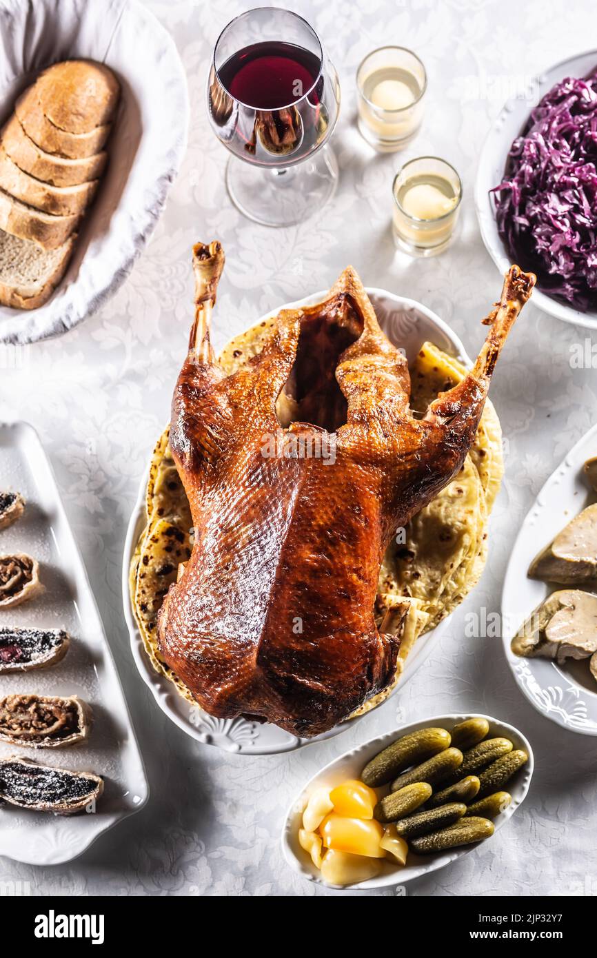 Roast goose with side dishes, red cabbage, roast, strudel, potato dumplings, pickles, bread and red wine. Traditional holiday food. Top view. Stock Photo