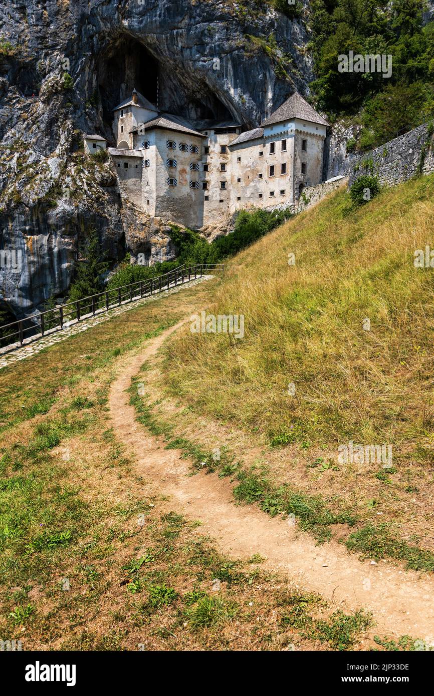 Predjama Castle in Slovenia, footpath in the meadow leading to medieval cave castle. Stock Photo