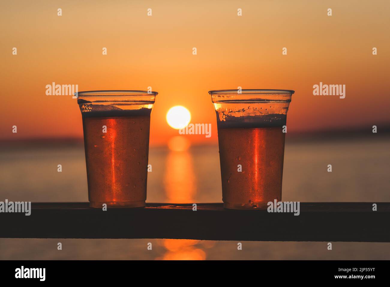 A bright orange sunset in the middle of two plastic cups of beer Stock Photo