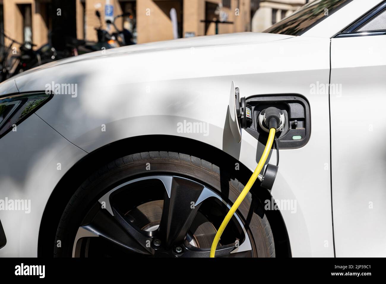 Close-up modern electric plug-in hybrid car parked near fast charger charging station point in center street old European city. Eco friendly green Stock Photo