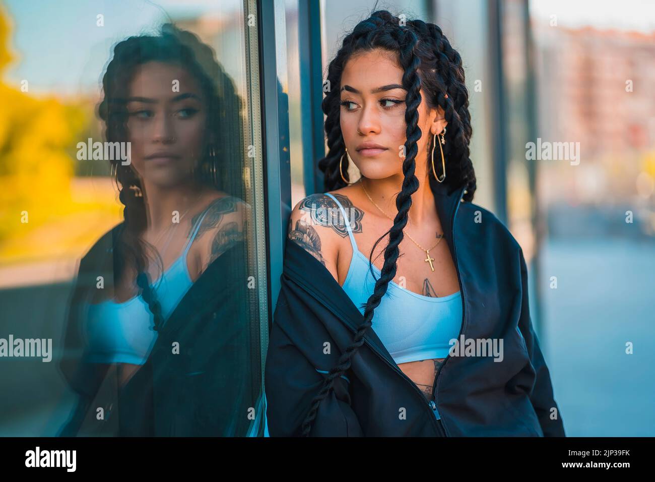 A young Hispanic woman with long braids and tattoos posing under the
