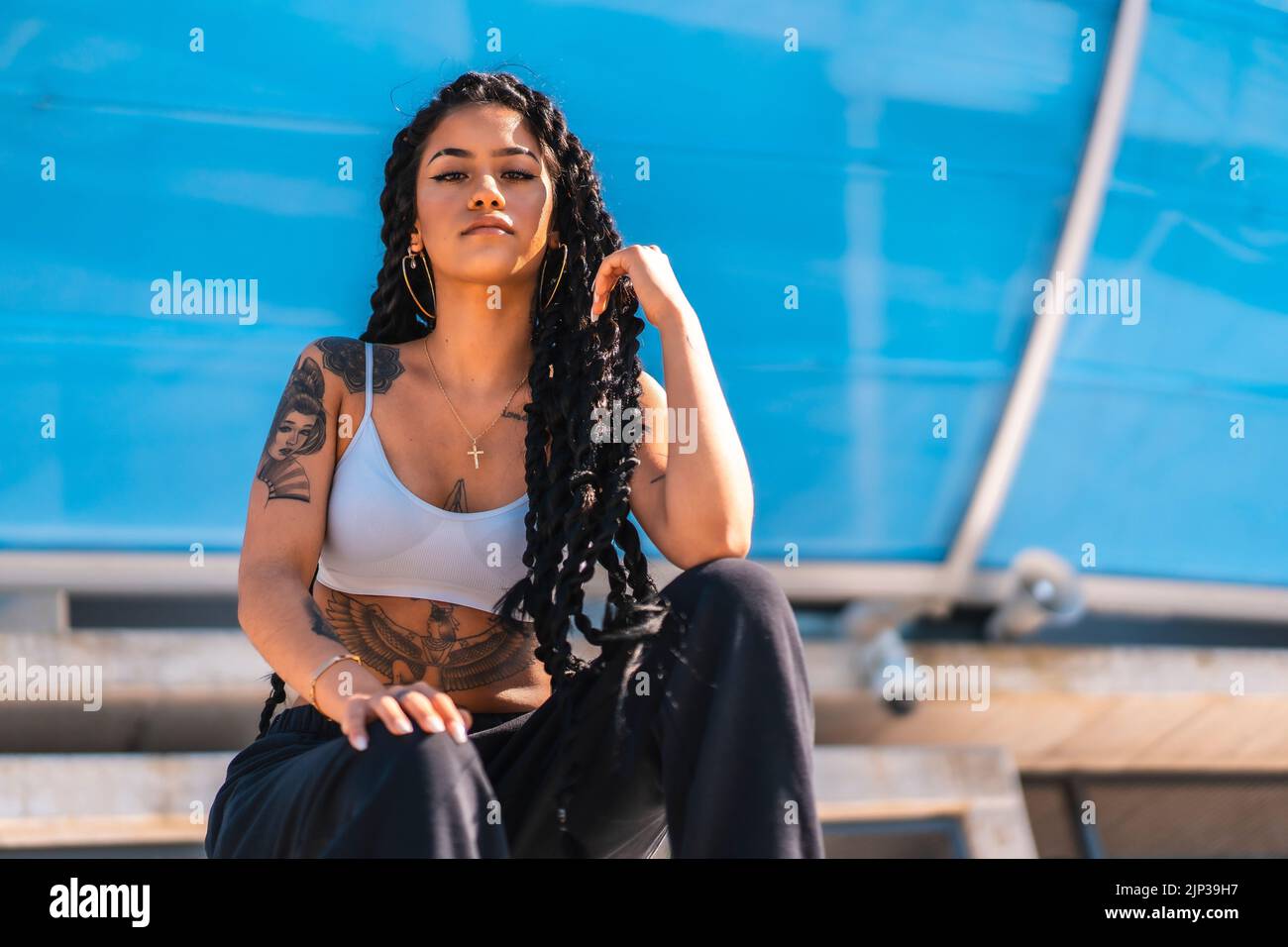 A young Hispanic woman with long braids and tattoos posing under the  sunlight Stock Photo - Alamy, image size:1300x956