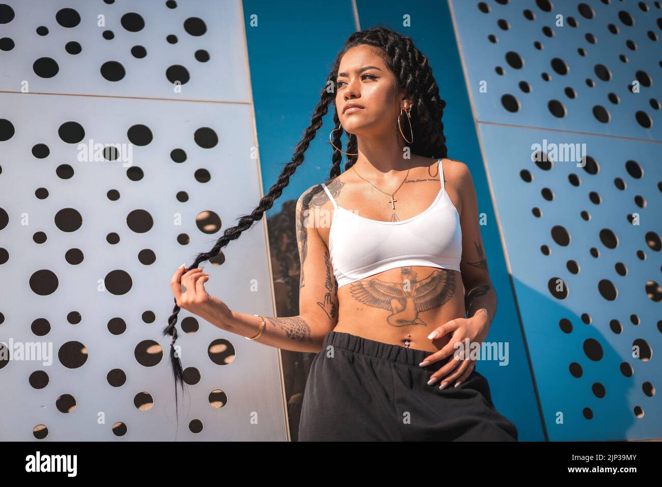 A young Hispanic woman with long braids and tattoos posing under the
