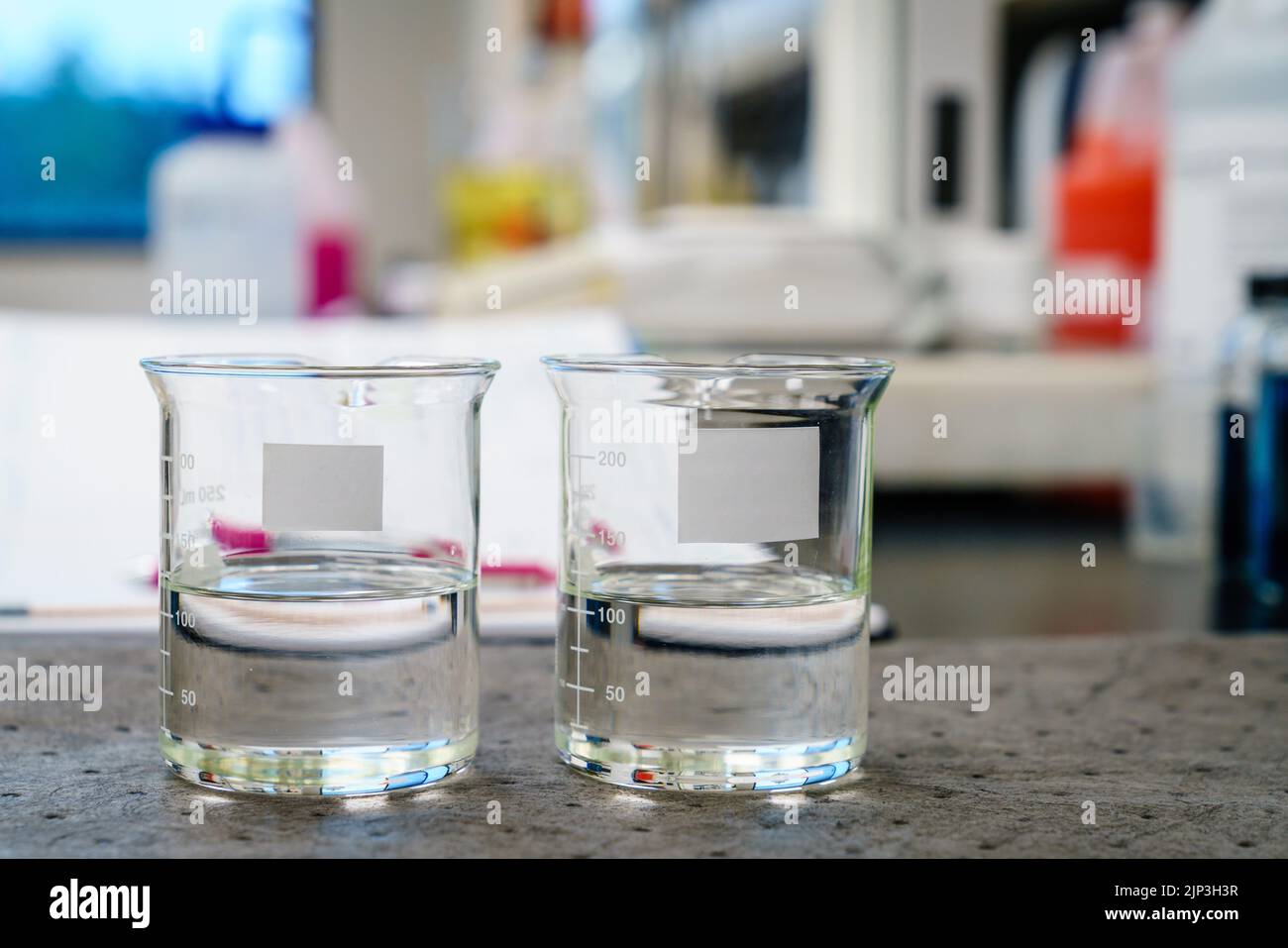 Two beakers with clear liquids and blank labels on a pad in a laboratory Stock Photo