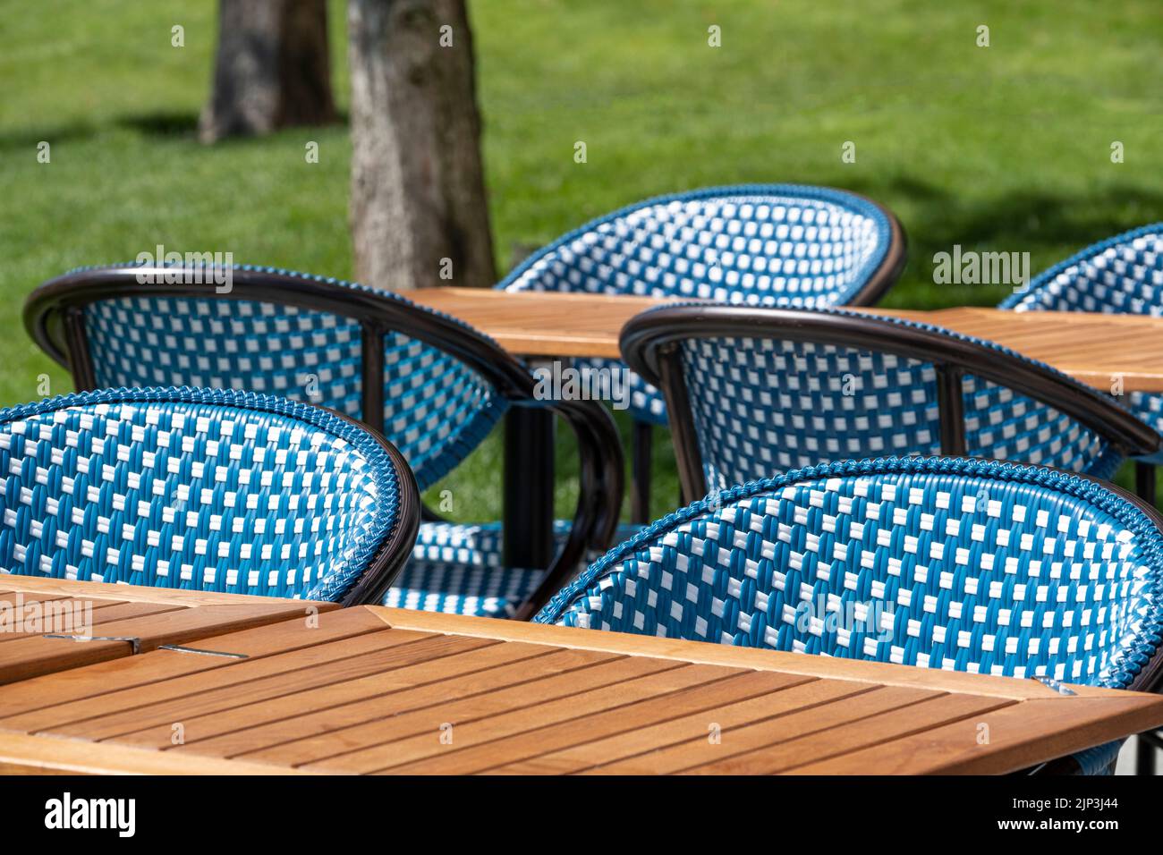 Outdoor cafe - restaurant tables and chairs, with no customers in a garden atmosphere in bright sunshine. Stock Photo
