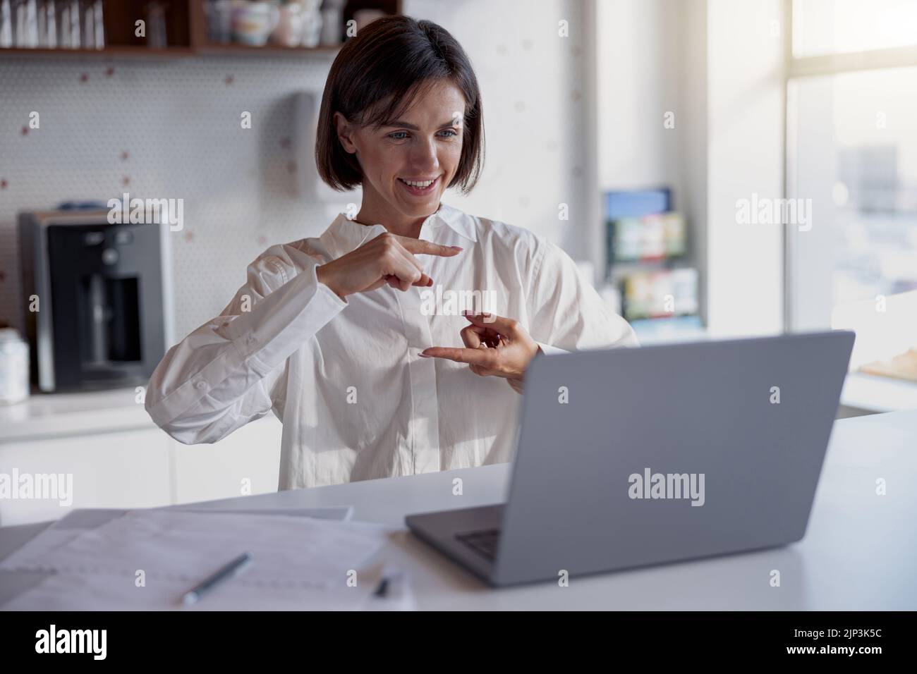 Smiling businesswoman making videocall to client while working in modern office Stock Photo