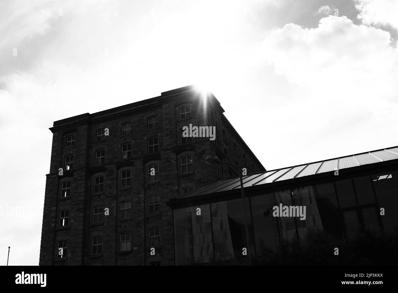 A grayscale of the sun shining behind an old stone building in Dublin, Ireland Stock Photo