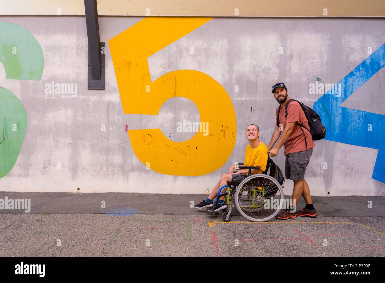 A disabled person in a wheelchair with a cement wall, walking with a