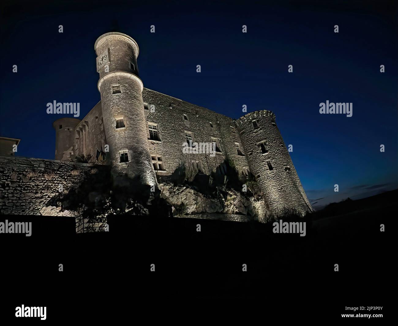 Night landscape photography on the old illuminated majestic castle at Lussan, Gard, France against a dark sky Stock Photo