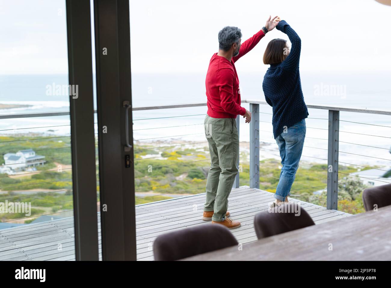 Diverse couple dancing and wearing jumpers together at balcony Stock Photo