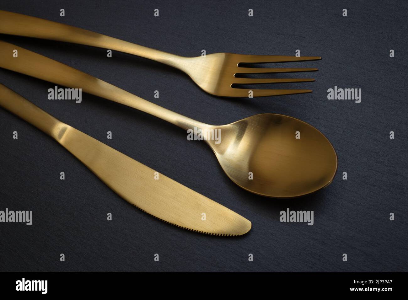 Gold knife, fork and spoon on a black stone background - Food concept photography Stock Photo