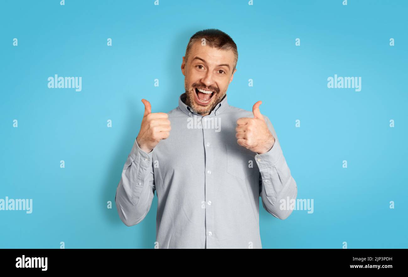 Joyful Middle Aged Male Gesturing Thumbs Up Over Blue Background Stock Photo