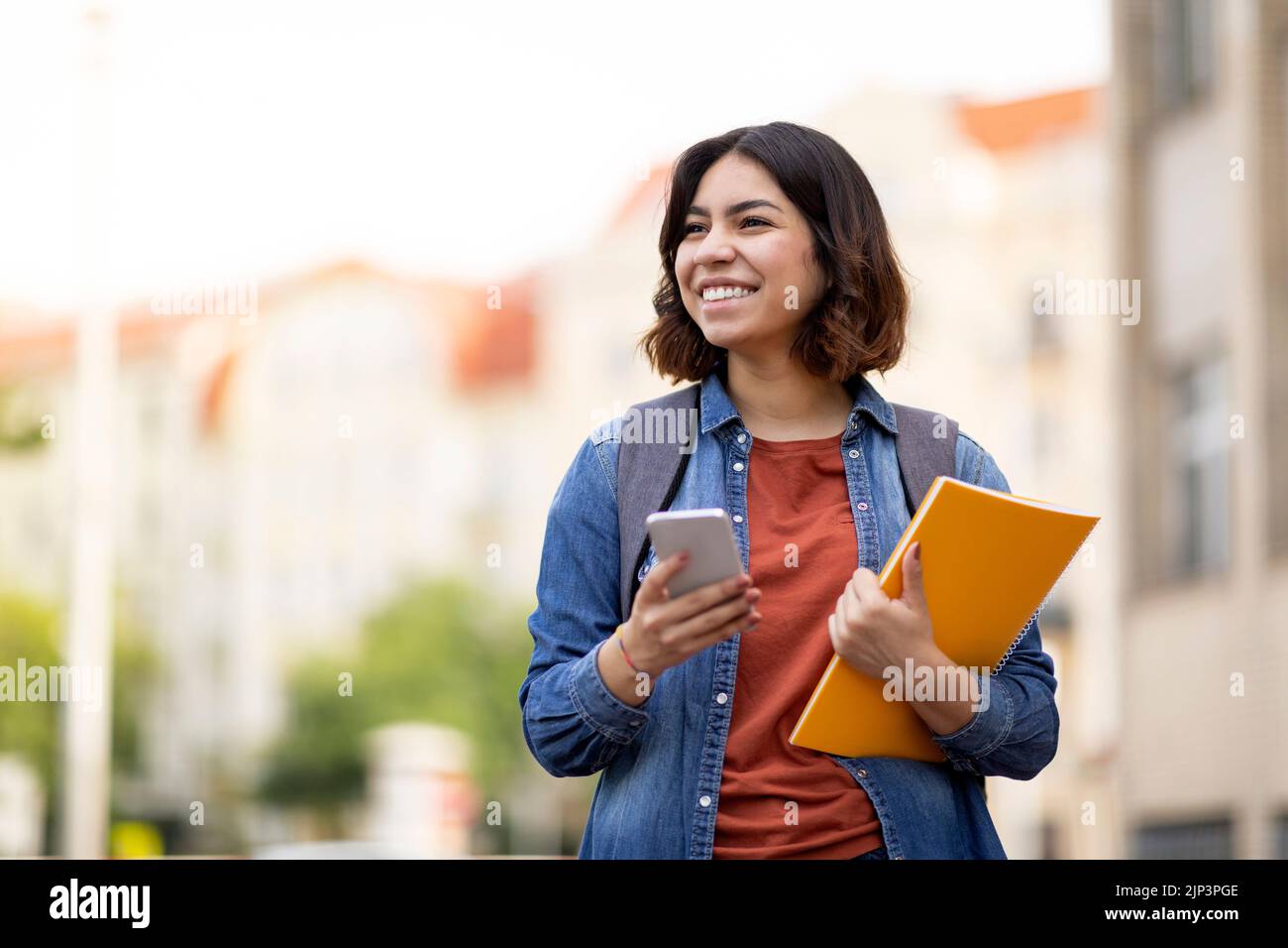 Cheerful Arab Female Student With Smartphone And Workbooks Standing Outdoors Stock Photo