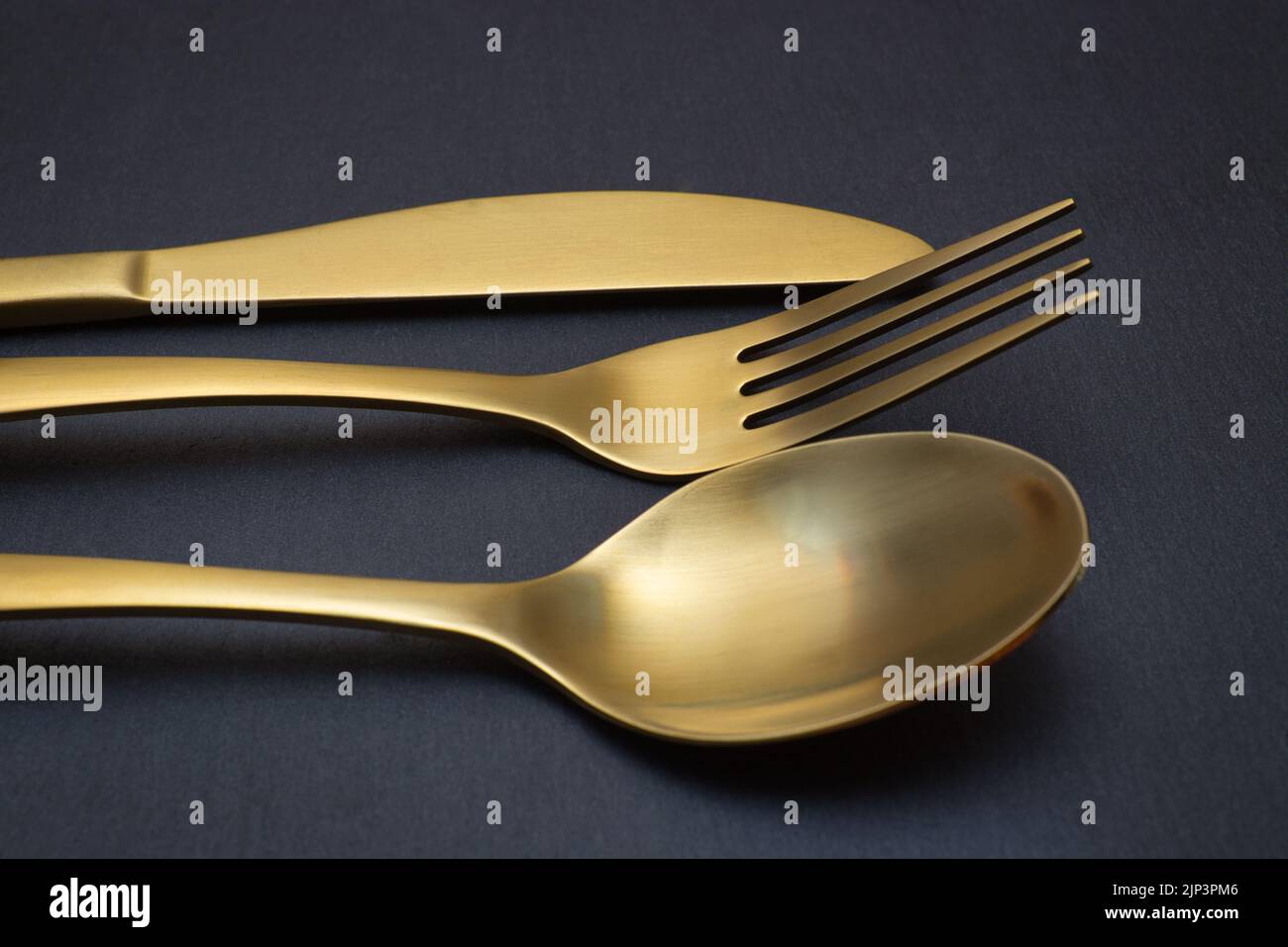 Gold knife, fork and spoon on a black stone background - Food concept photography Stock Photo