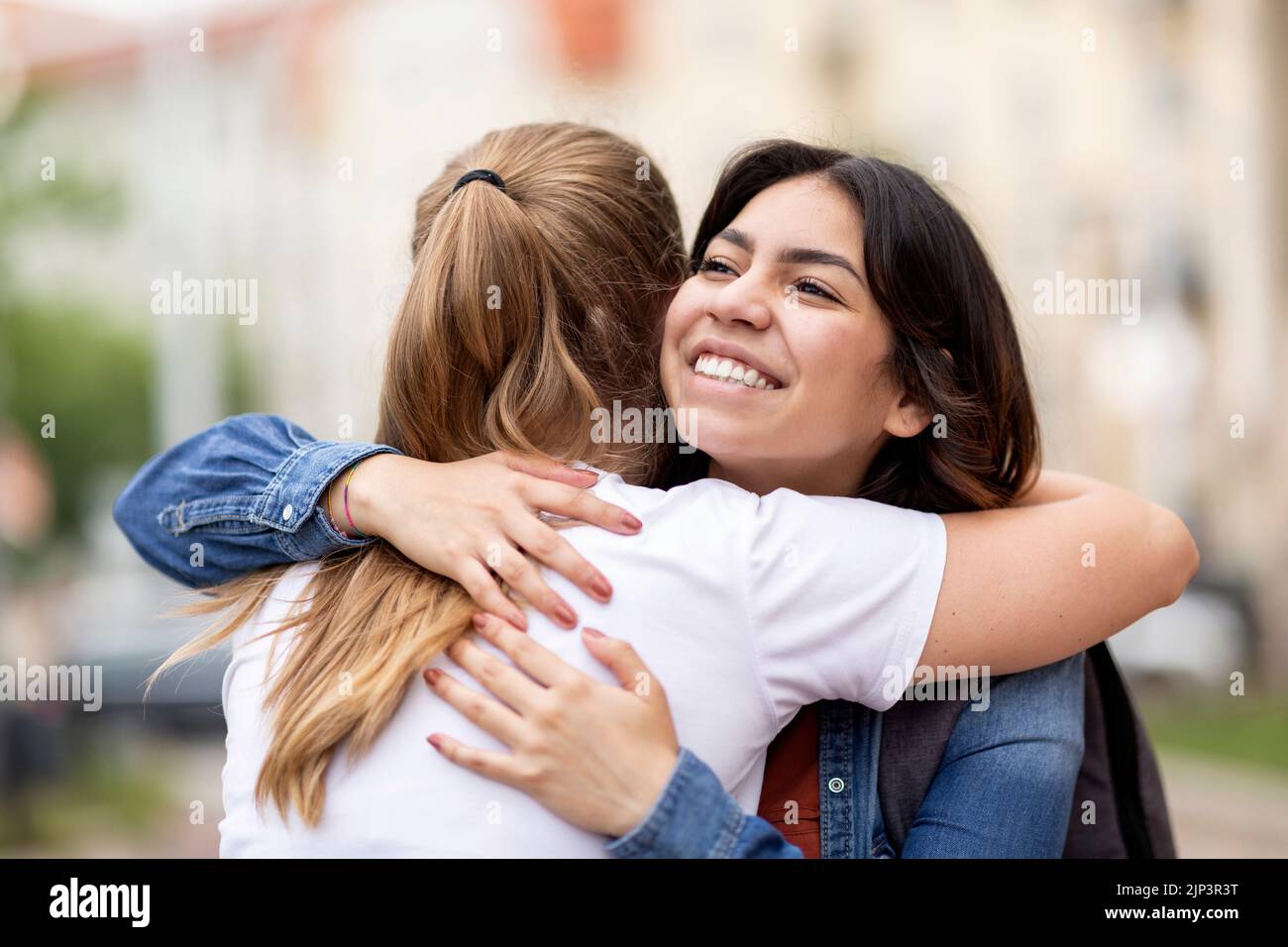 Friendship Concept. Two Happy Young Female Friends Embracing Outdoors On City Street Stock Photo