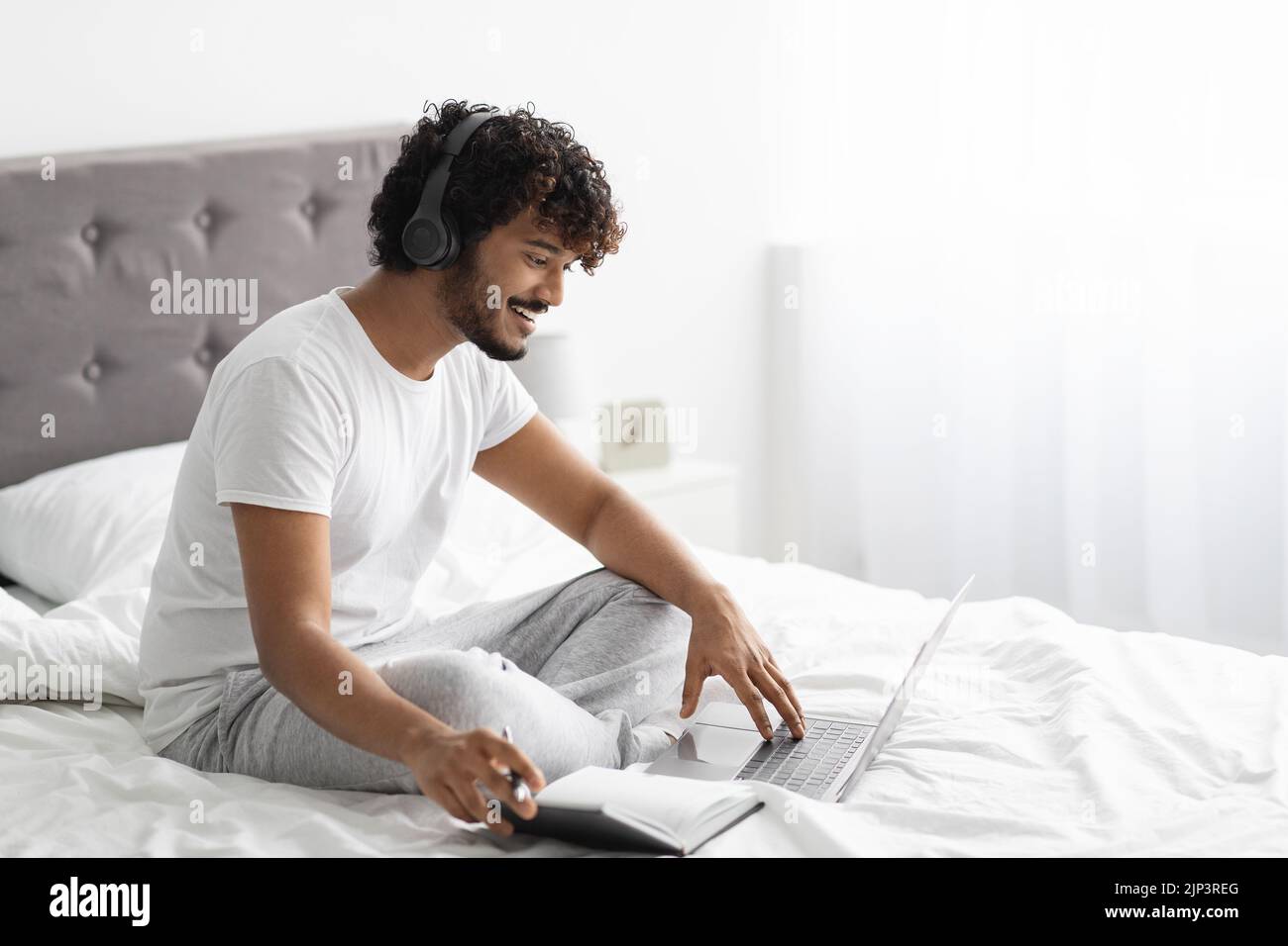Happy eastern guy studying in bed, using laptop Stock Photo