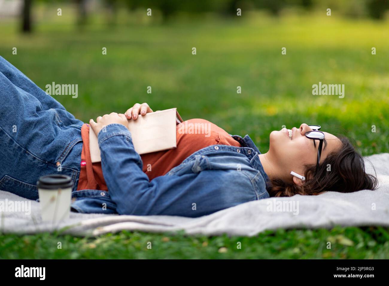 Young Arab Woman Relaxing On Lawn In Park With Book And Earphones Stock Photo